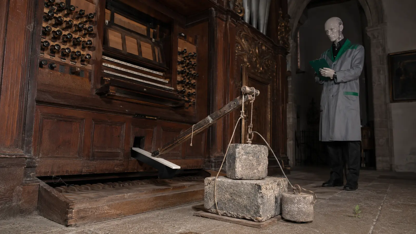 Steingewichte halten über einen Hebel eine Orgeltaste in einer alten Kirche gedrückt.